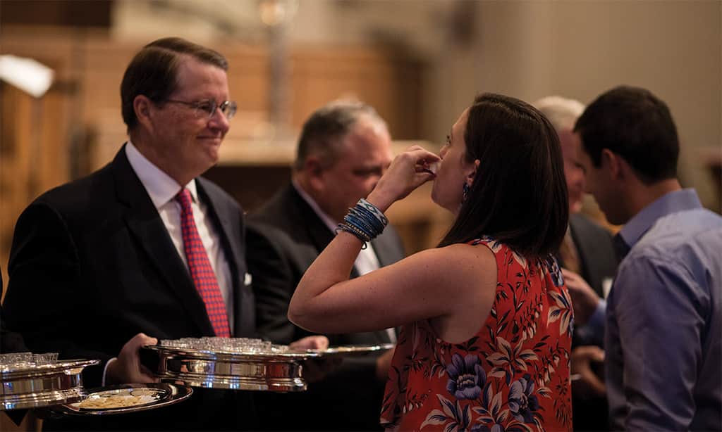 Woman receiving communion bread from a church leader holding a silver tray during a worship service.