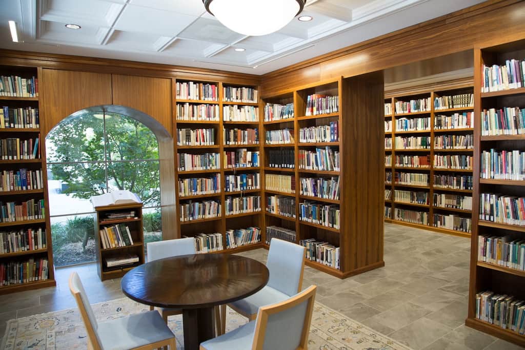 Adult church library with wooden bookshelves filled with books, a reading table, and an arched window.