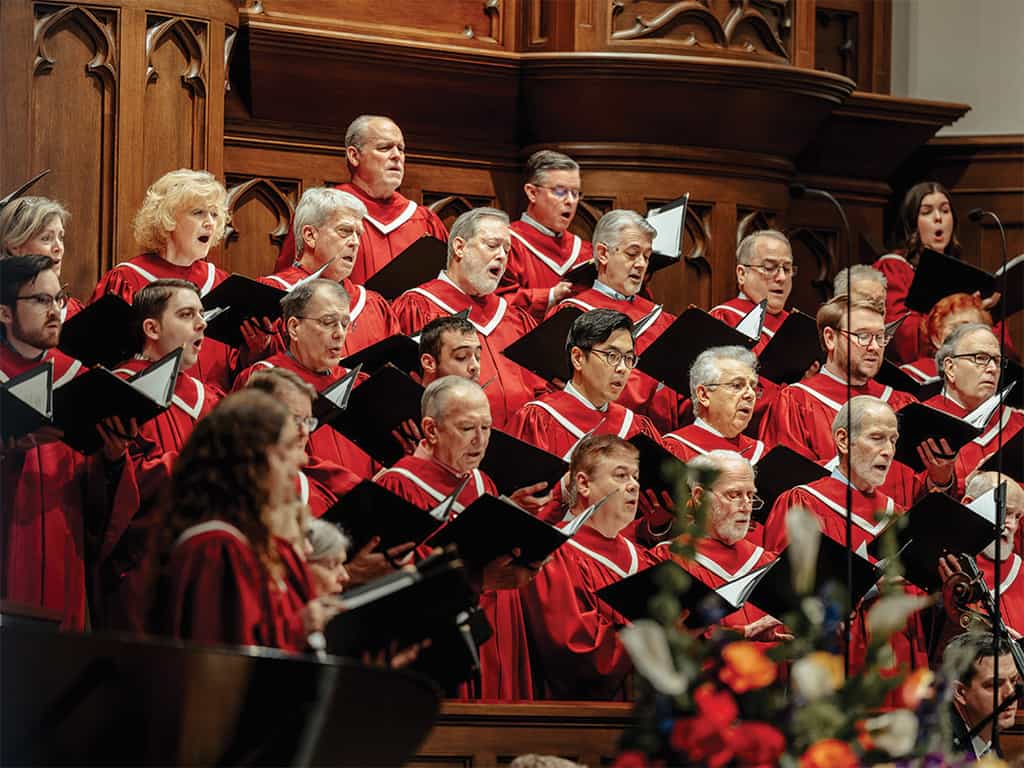 Traditional church choir in red robes singing during a worship service in a wood-paneled sanctuary.