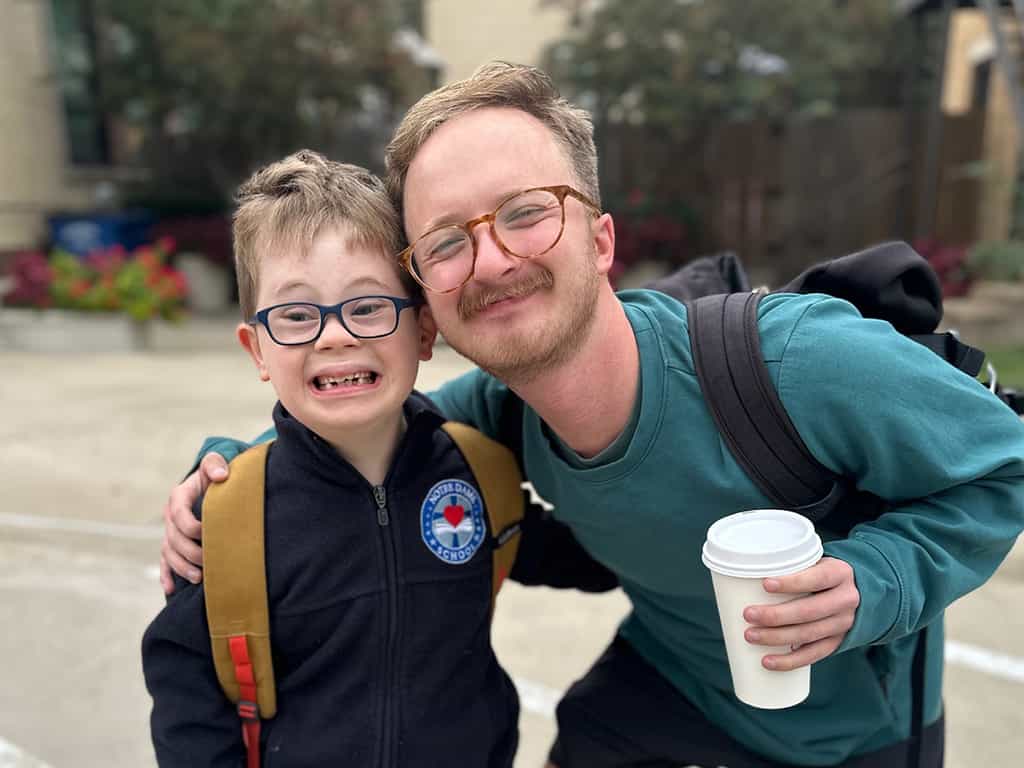 A young man and a boy wearing glasses and a backpack outside a church with a Special Needs Ministry.