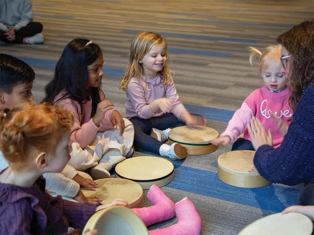 Preschool children sitting in a circle playing hand drums together during a music class.