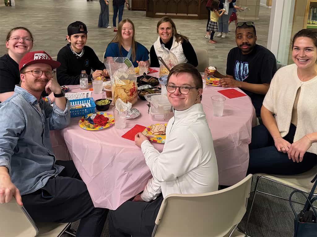 Group of adults and young adults sharing a meal together at a table during a Special Needs Ministry gathering.