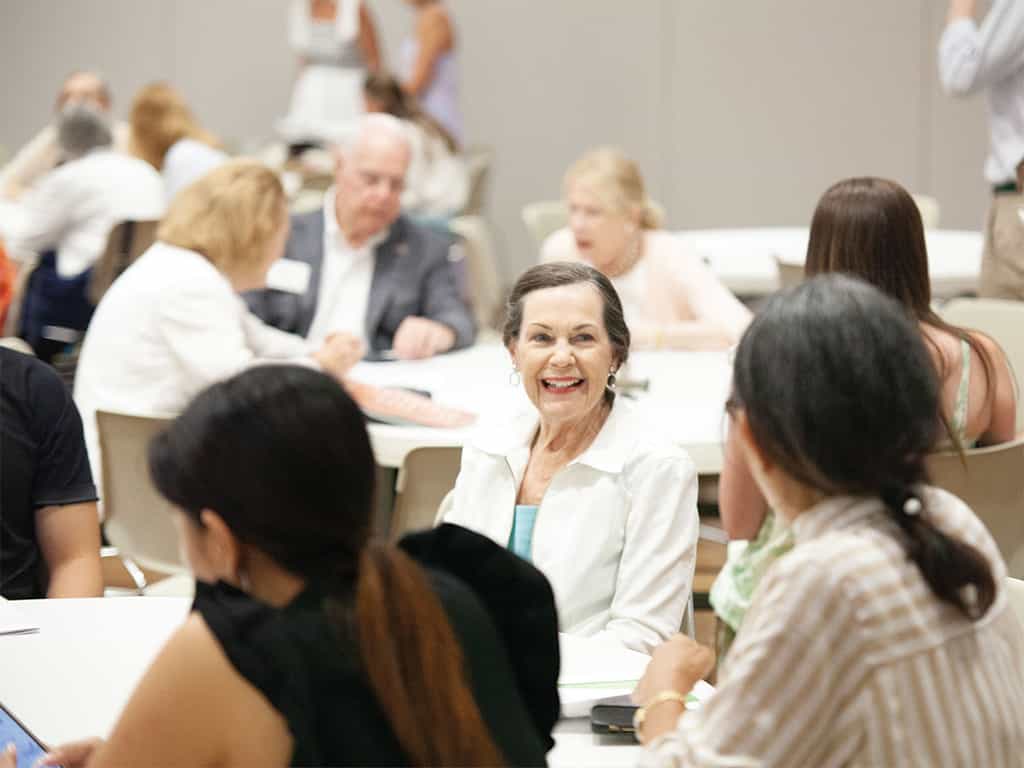 Adults seated around tables talking and smiling during a church class or group discussion.