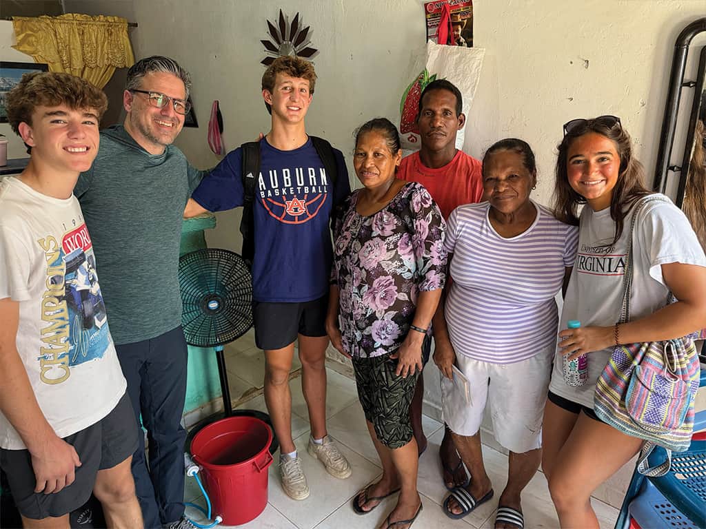 Small group of mission trip volunteers standing with a local family inside a home during a service project visit.