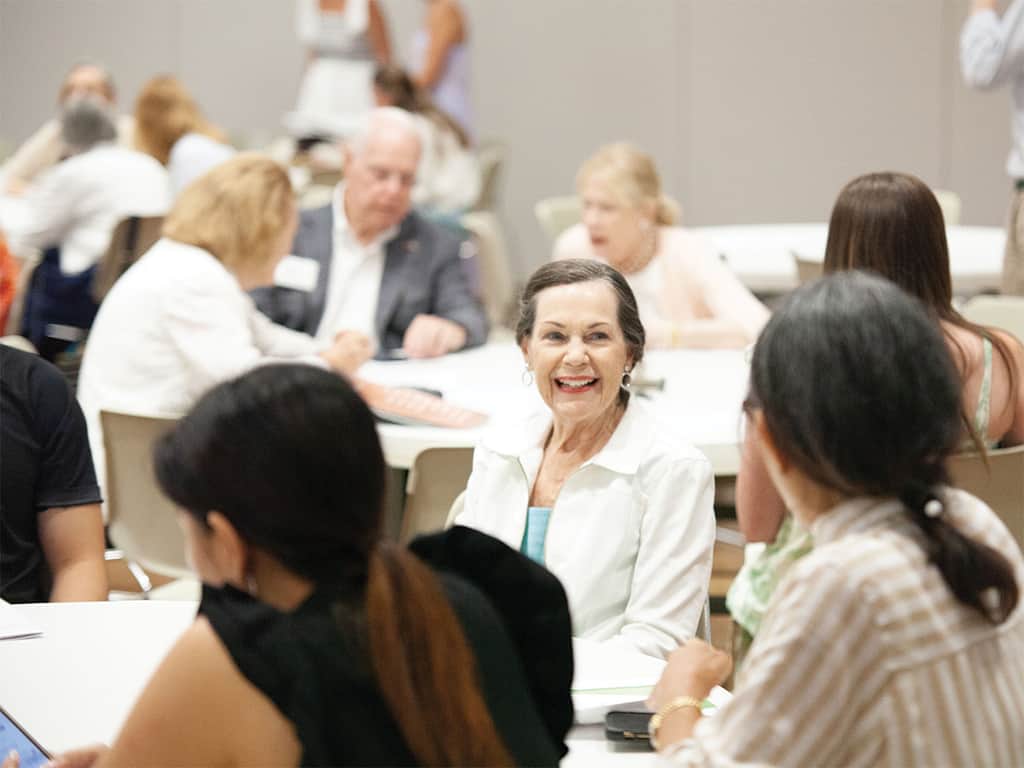 Adults seated around tables talking and smiling during a church class or group discussion.