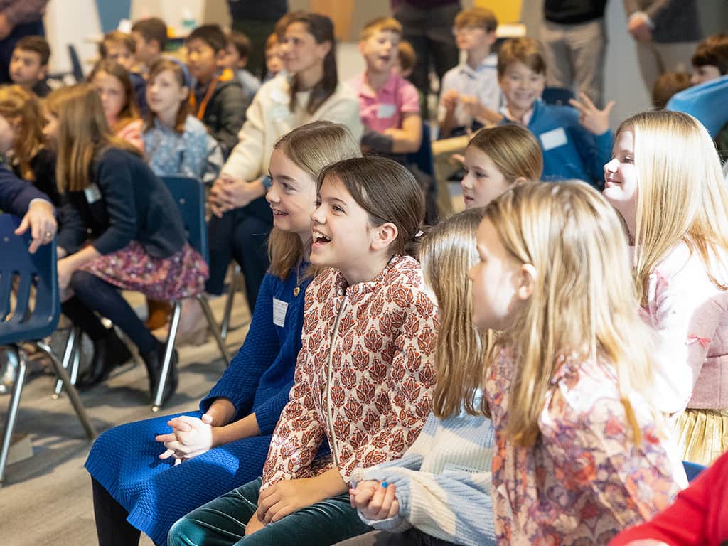Elementary-aged children smiling and listening during a church kids ministry gathering.