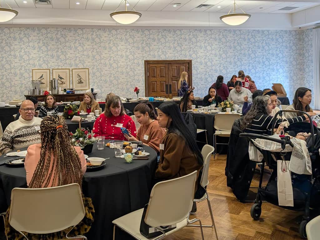 Church fellowship meal with adults gathered around round tables indoors.