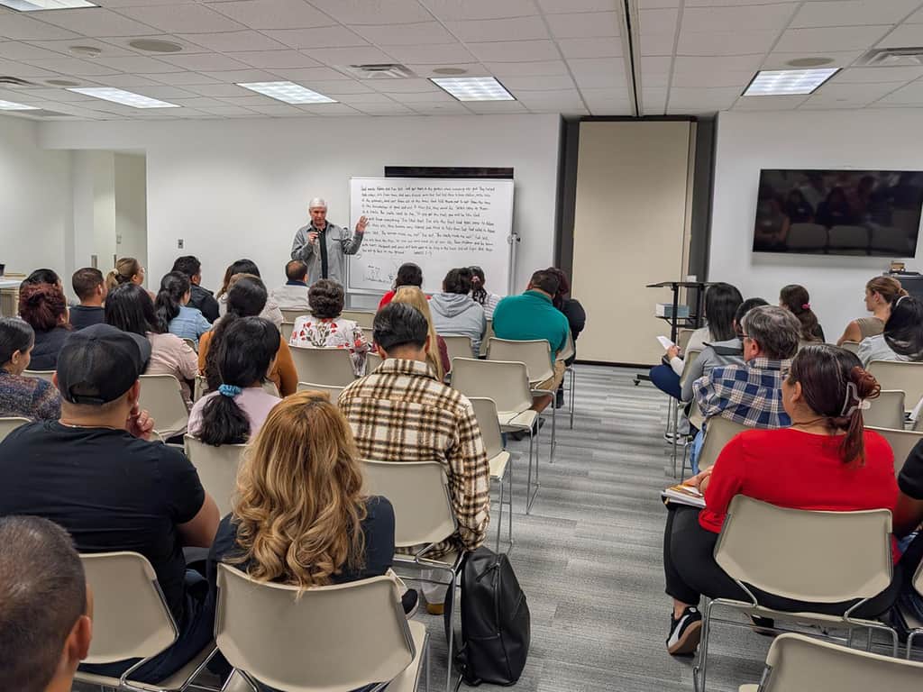 Large adult Bible study class listening to teacher at whiteboard.