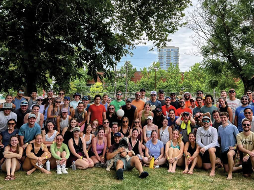 Large group of young adults gathered outdoors in a park, smiling together for a group photo.