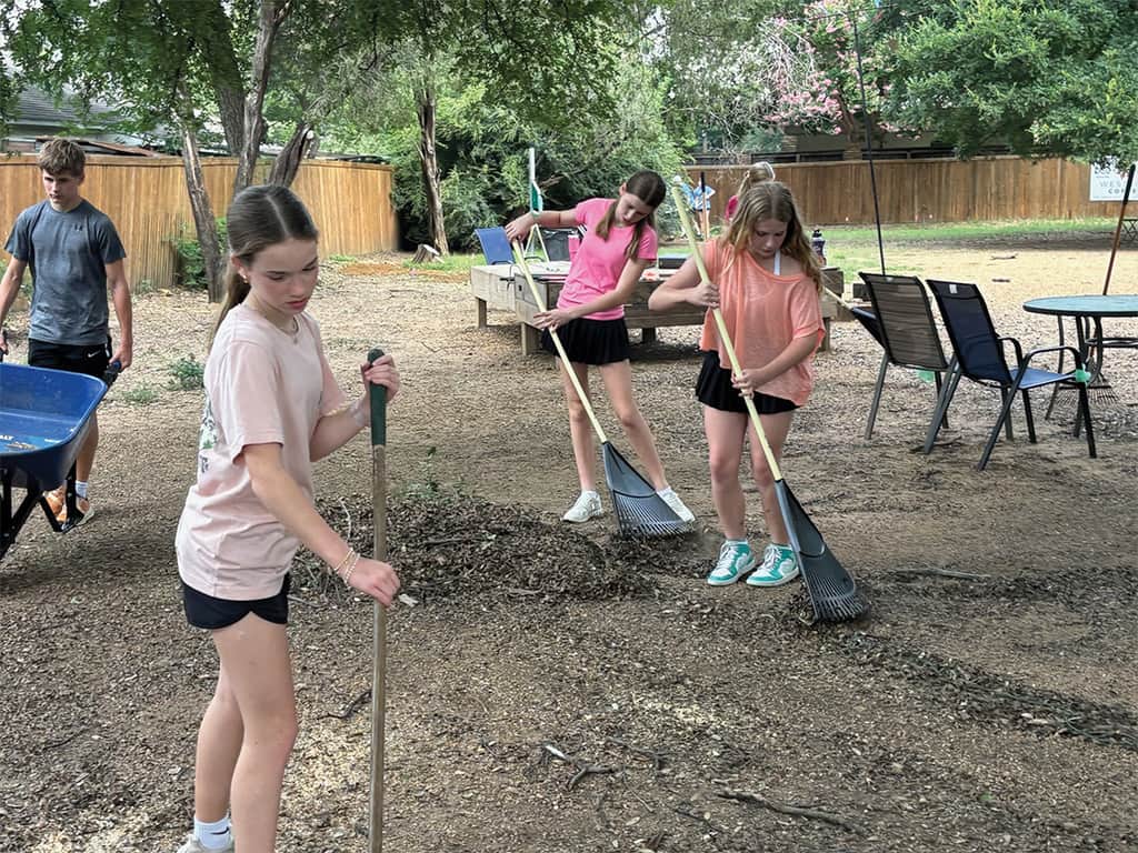 Teens working together outdoors raking leaves and clearing debris during a service project.