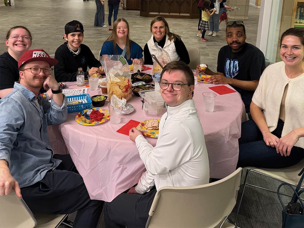 Group of adults and young adults sharing a meal together at a table during a Special Needs Ministry gathering.