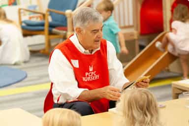 Preschool volunteer reading to young children in a nursery classroom setting.