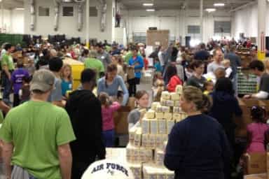Large group of volunteers packing food supplies together inside a warehouse.
