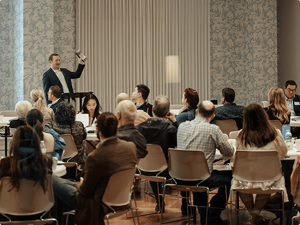 Teacher speaking at the front of a room to adults seated at tables during Sunday school classes in Dallas.