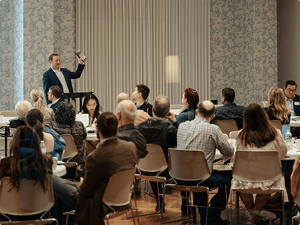 Teacher speaking at the front of a room to adults seated at tables during Sunday school classes in Dallas.