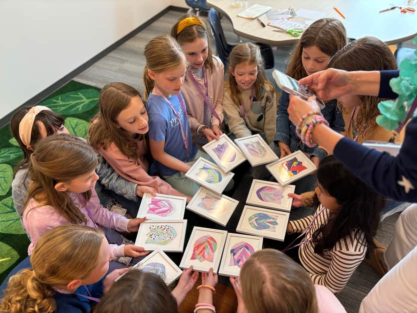 Children in a classroom circle holding framed heart artwork during a kids ministry craft activity.